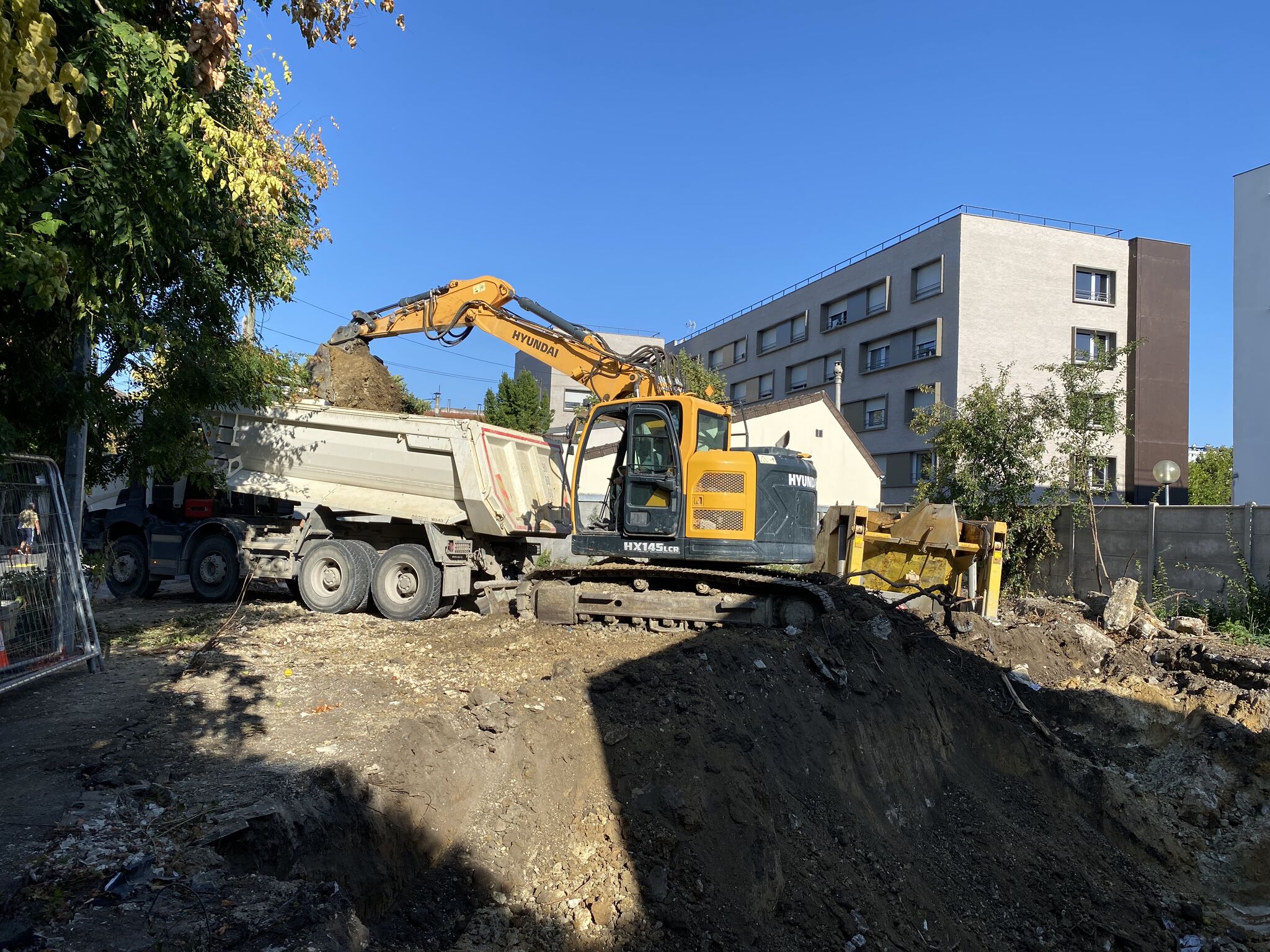 Pelle mécanique et camion-benne en cours de terrassement au pied d'un immeuble