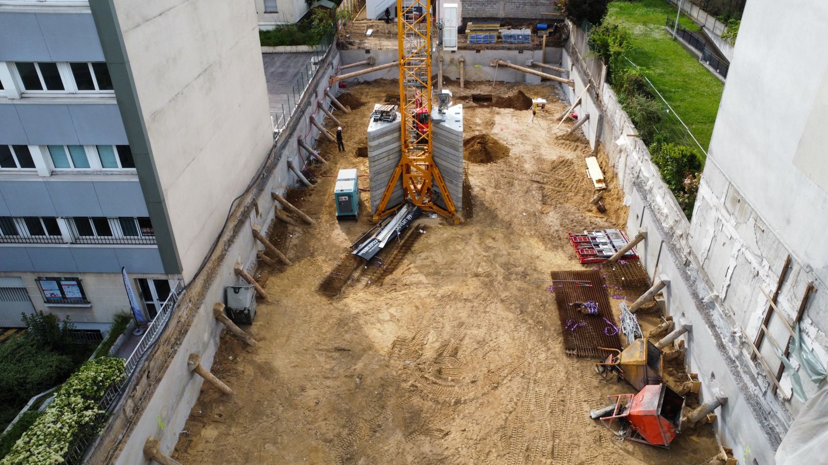 Vue aérienne d'une fouille entre deux immeubles, grue à tour et engins de terrassement